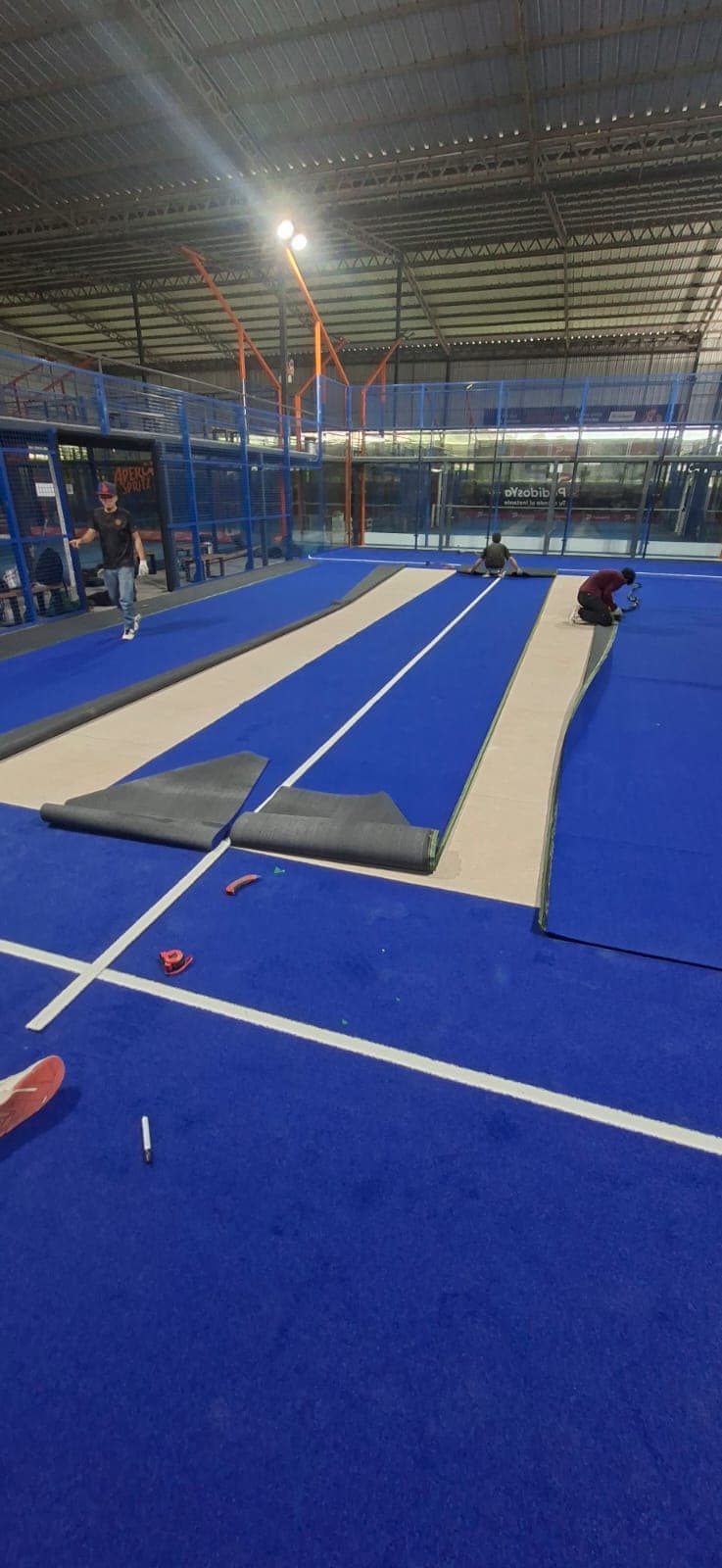 Colocación de césped sintético en cancha de pádel techada.
